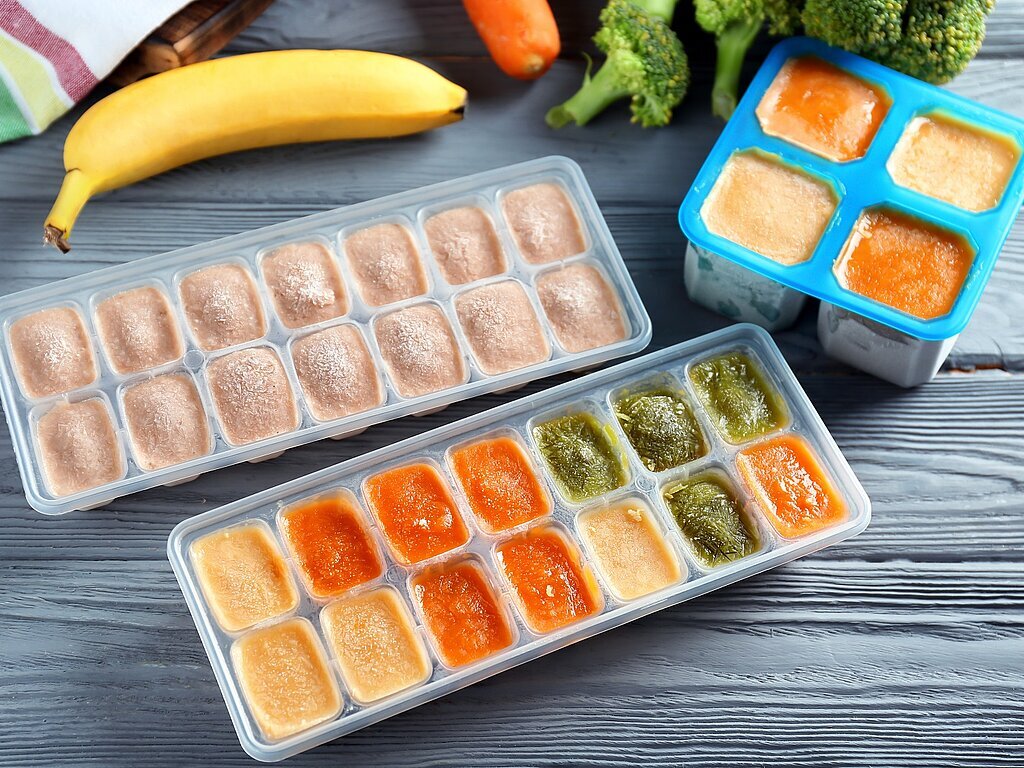 Ice trays with frozen vegetable and fruit puree on wooden table